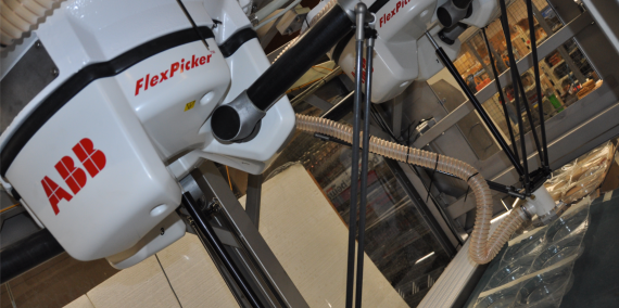 Two ABB FlexPicker robotic arms in operation, enclosed within a workspace.