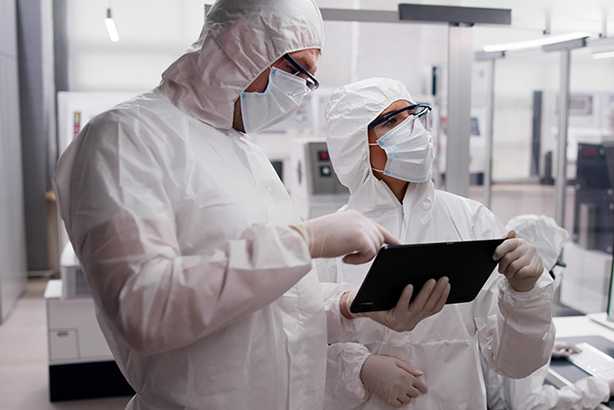 Scientists in protective suits analyze data on a tablet in a laboratory setting.