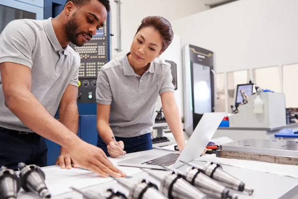 Engineers collaborating on project in modern manufacturing facility with machinery and tools visible on the table.