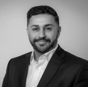 Man in a suit with a beard and dark hair, smiling at the camera